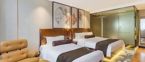 A modern hotel room with two beds, a sofa, a glass partition, and a world map artwork on the wall.