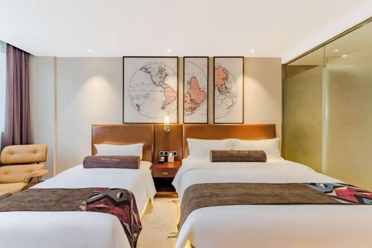 Quarto de hotel com duas camas, uma mesa de cabeceira, um abajur e uma janela grande.