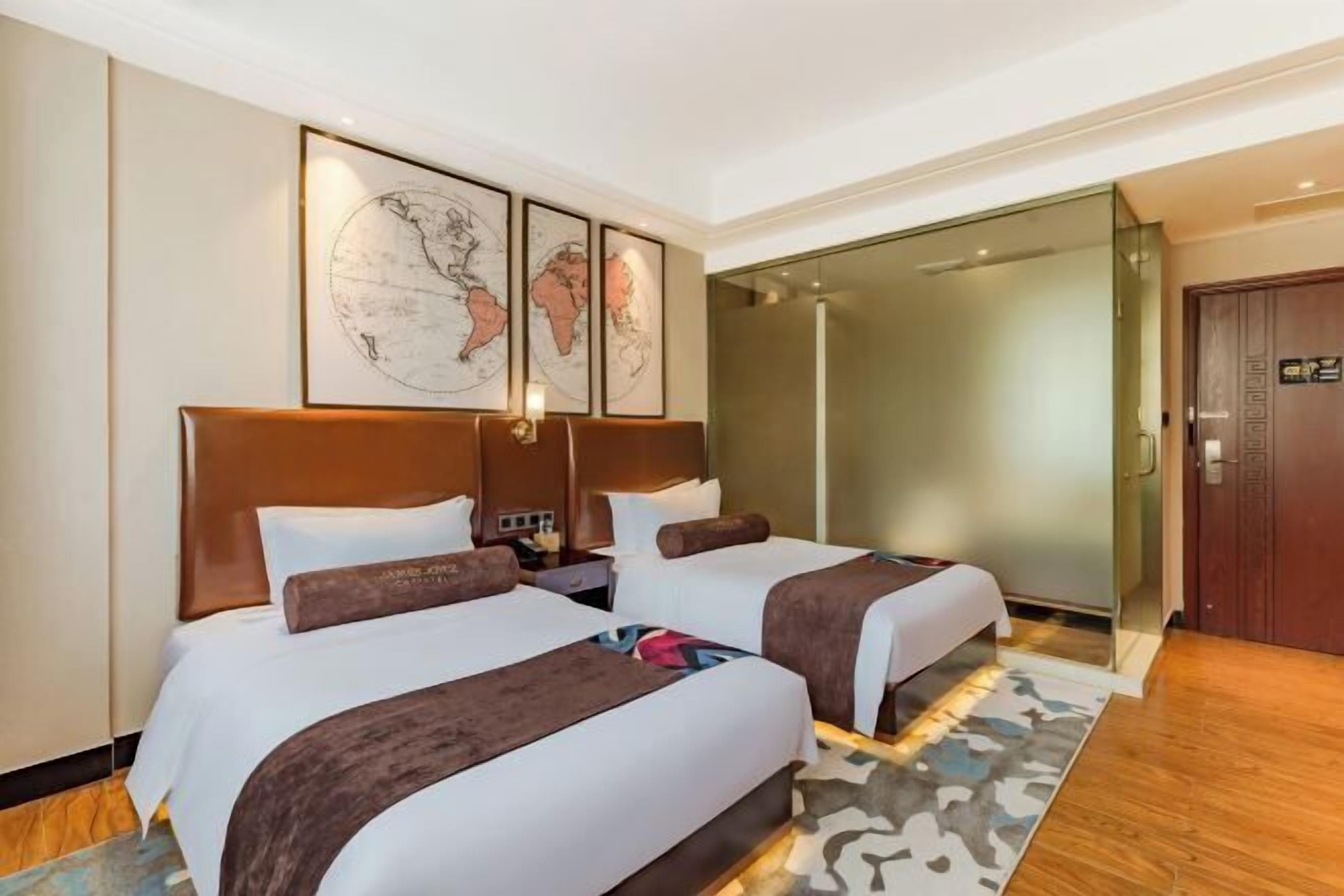 A hotel room with two beds, a world map on the wall, a glass shower enclosure, and a wooden floor.