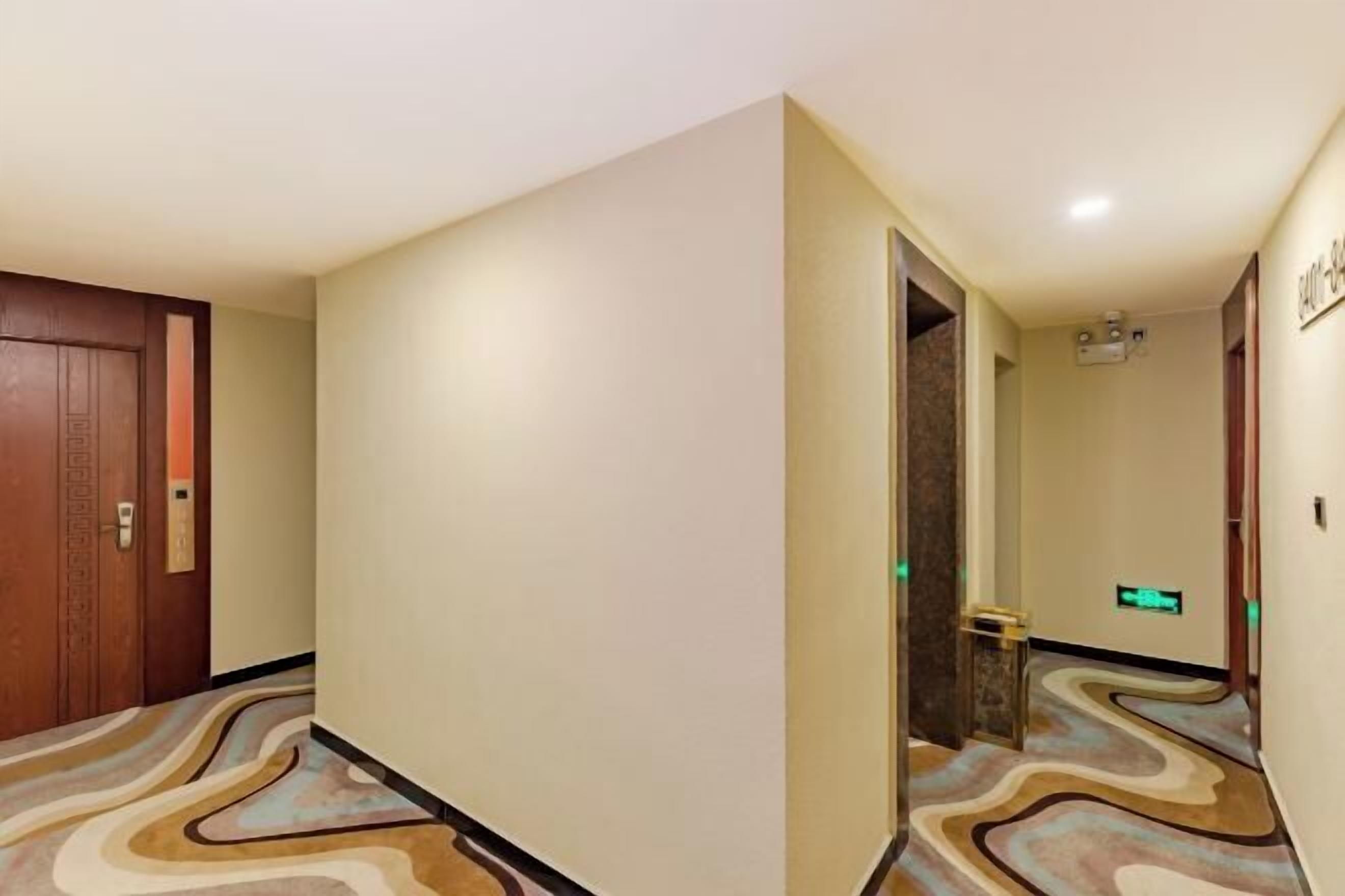 Pasillo de hotel con alfombra estampada, una puerta de madera y una lámpara fijada a la pared.