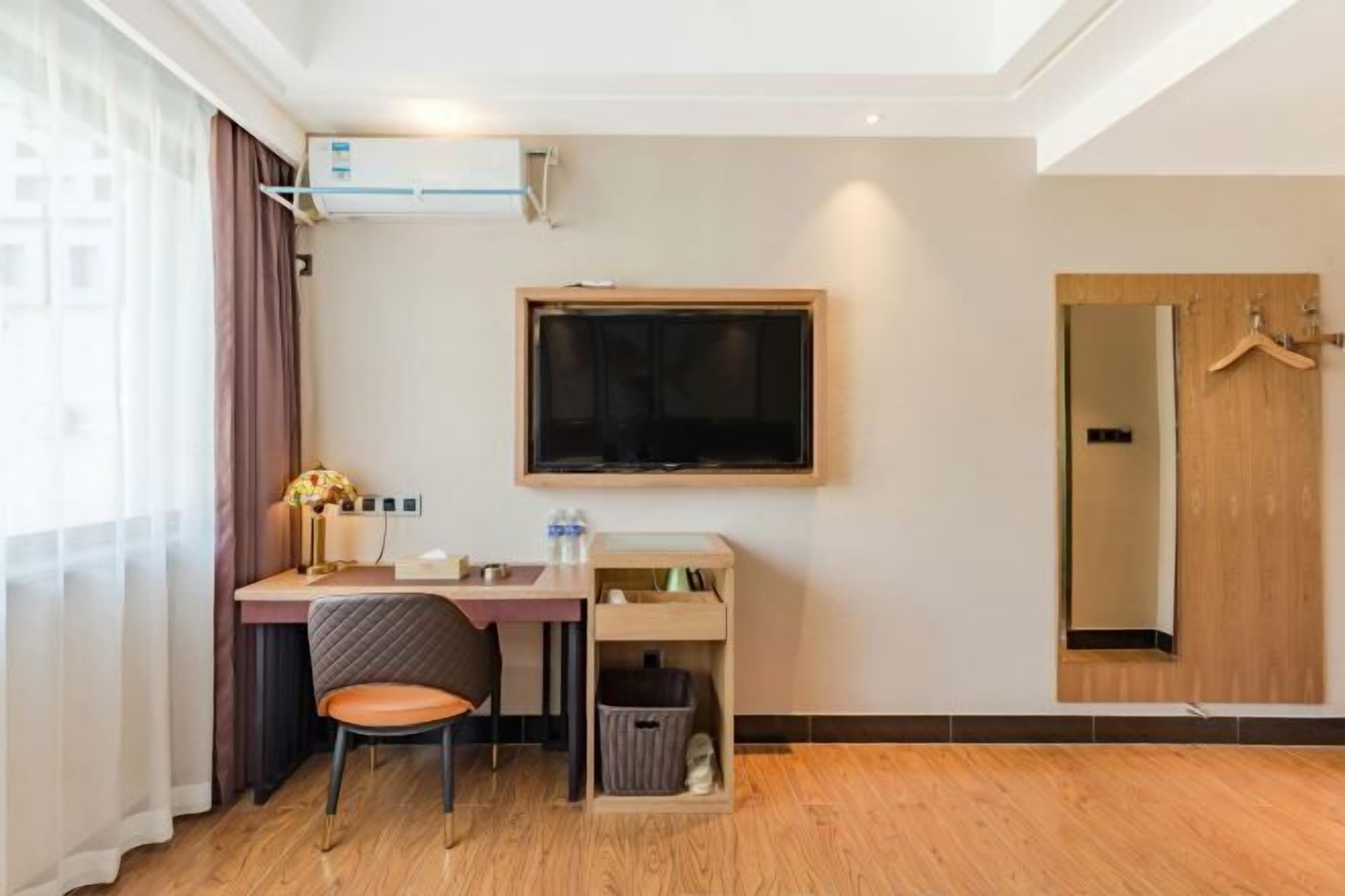 Habitación de hotel con escritorio, silla, televisor y puerta de madera.