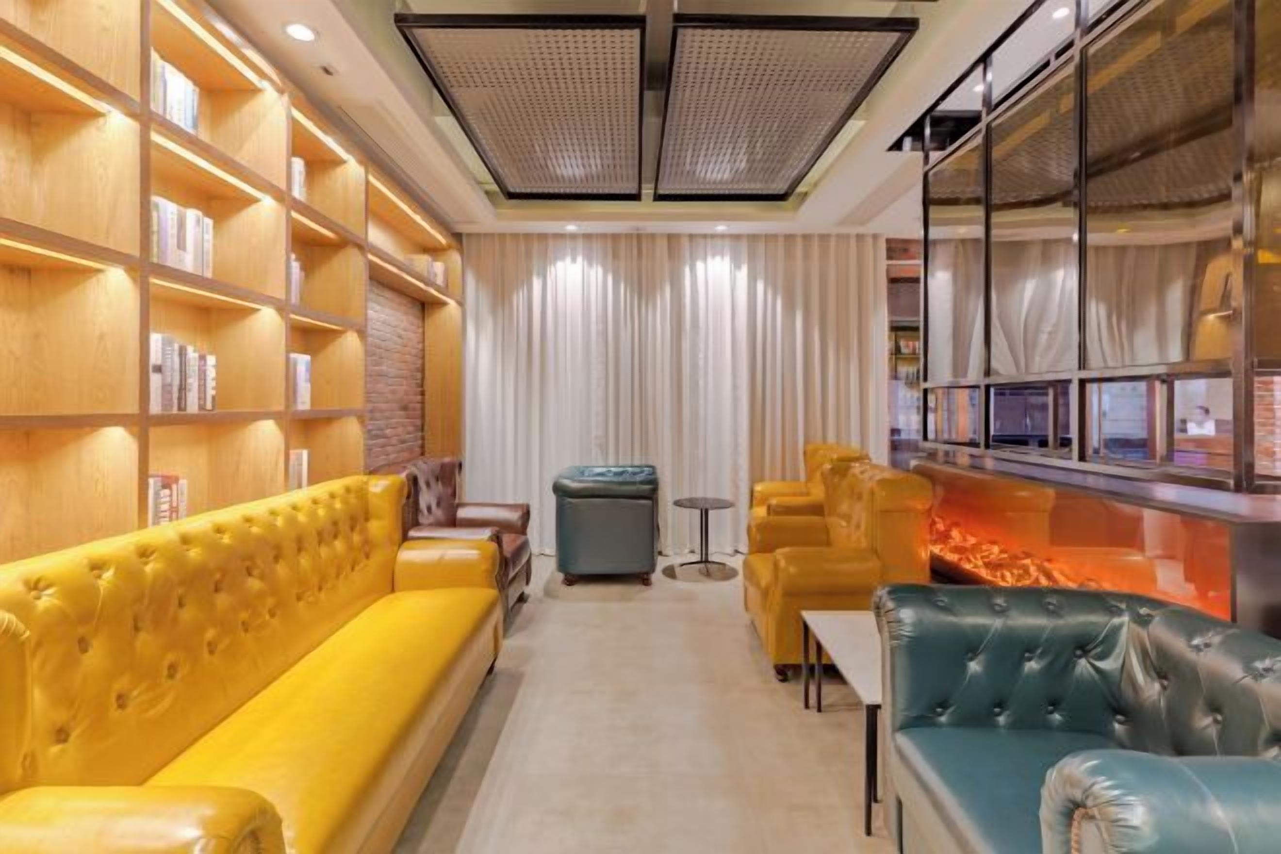 Un intérieur moderne avec un canapé jaune, un canapé vert et un pouf bleu. On trouve des étagères à gauche et un coin bar à droite.