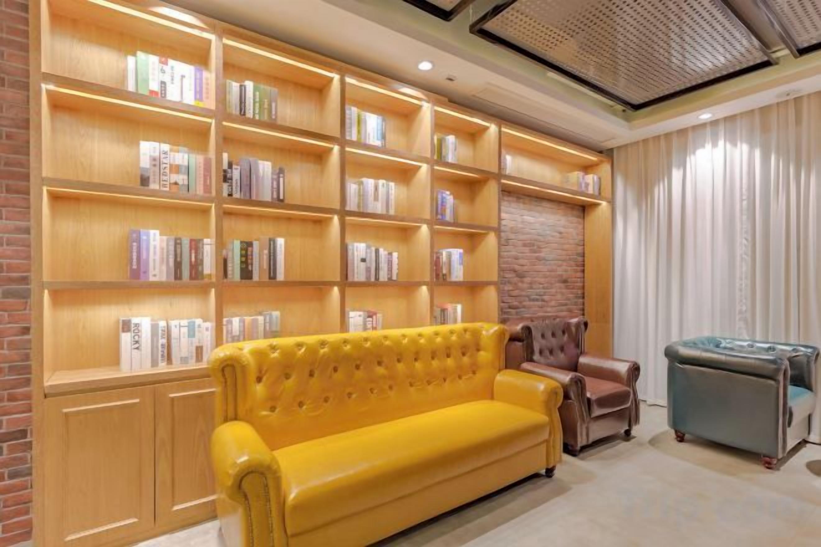 A room with a large bookshelf, a yellow sofa, a brown armchair, and a blue ottoman.