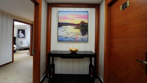 Habitació d'hotel amb una porta de fusta, un quadre amb un capvespre sobre un riu i una taula de console negra amb un bol a sobre.
