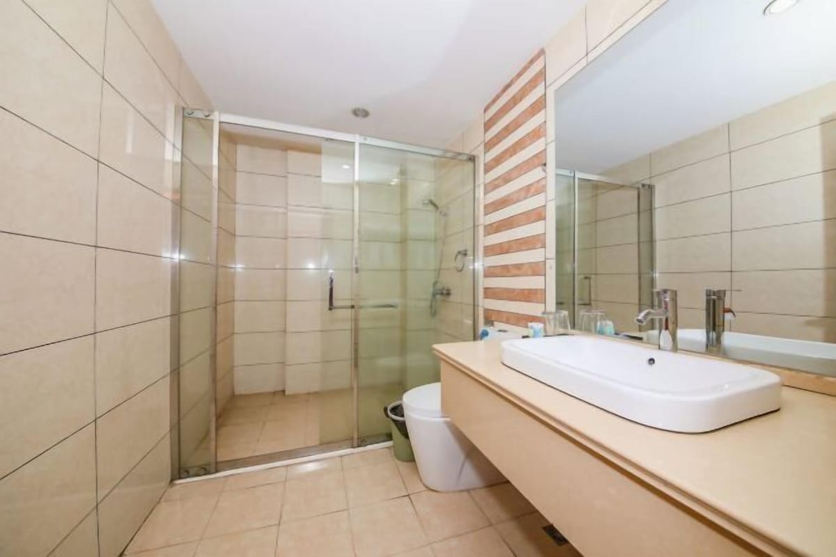 Un bany modern amb una dutxa envidriada, un mirall gran i un moble de tocador beix amb un lavabo blanc.