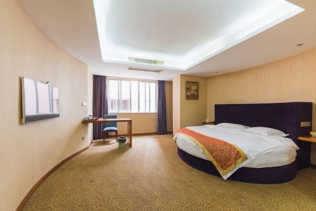 Habitació d'hotel amb llit, escriptori, cadira, televisió i finestra amb cortines.