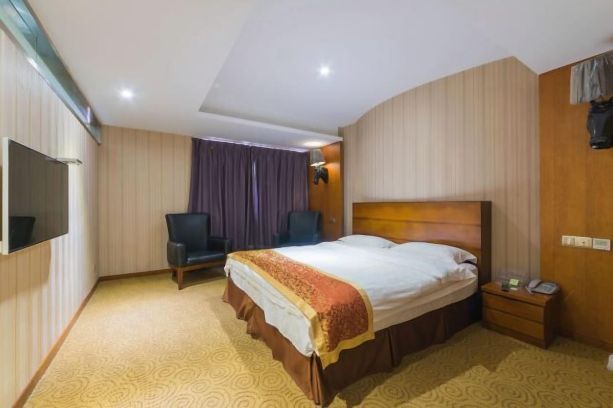 Habitació d'hotel amb llit, cadira, escriptori, telèfon i televisió.