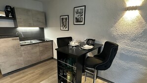 A compact kitchen with modern appliances, a dining area with two black chairs, and a bar area with a wine cooler.