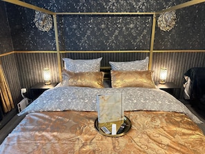 Una habitación de hotel con una cama grande, dos mesitas de noche, un cabecero y una lámpara de pared.