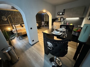 Una cucina moderna con zona pranzo, che include una sedia nera dal design decorativo, un forno a microonde e una macchina da caffè.