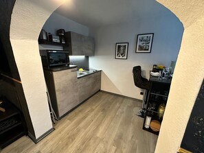 A compact kitchen with a microwave, sink, and a small countertop. There are framed pictures on the wall and a bar area with glasses and bottles.