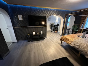A modern bedroom with a large bed, a TV mounted on the wall, and a small desk with a chair.