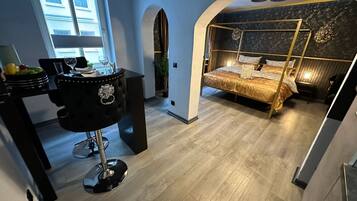 A modern bedroom with a bed, a desk, and a chair. There is a window and a door.