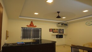 A reception area with a dark reception desk, a clock, and framed pictures on the wall. - Sri Srinivasa Residency (Puducherry)