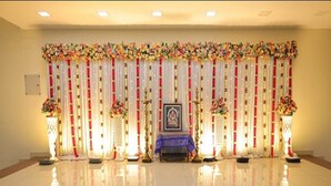 A stage with a framed picture, floral decorations, and two side tables with candles. - Sri Srinivasa Residency (Puducherry)