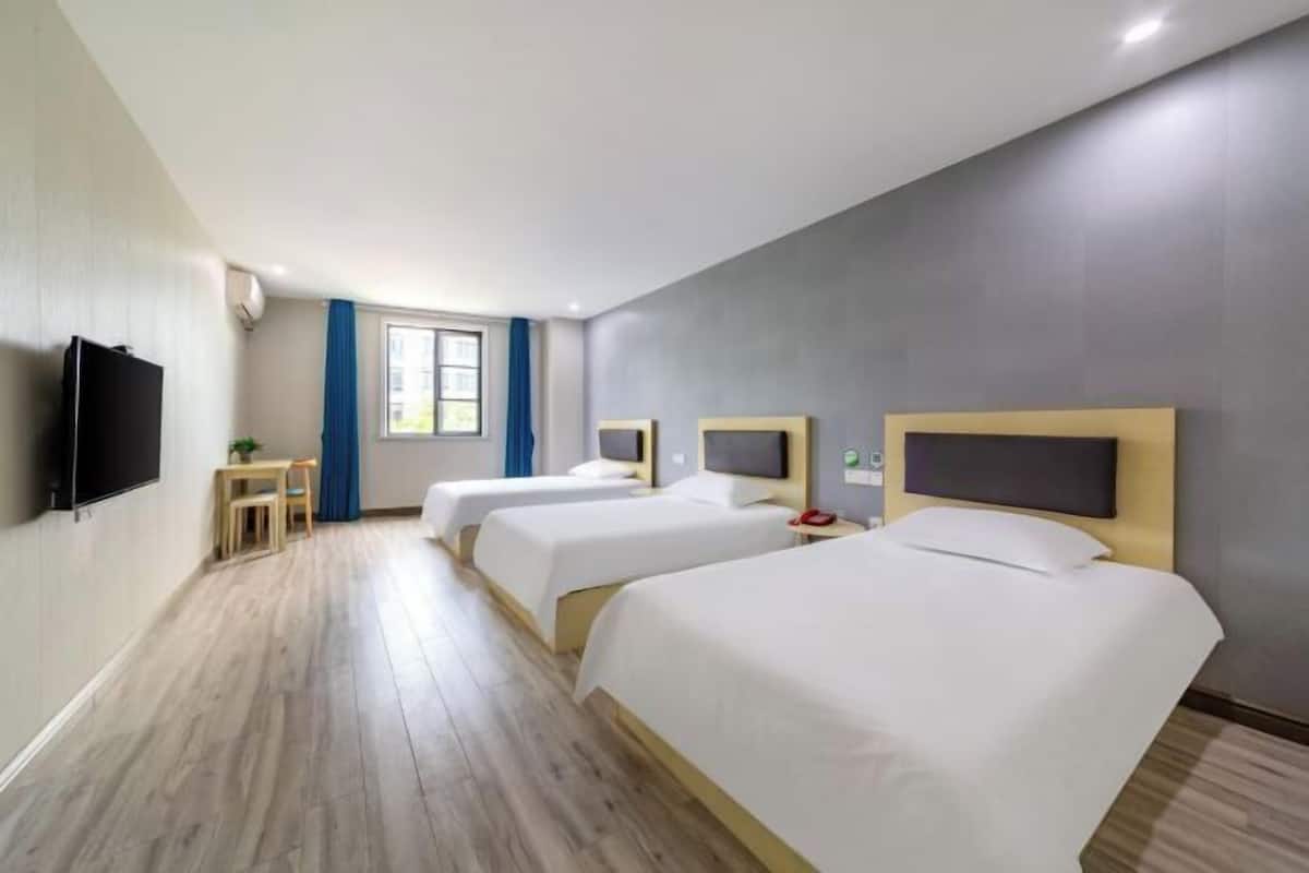 A hotel room with two beds, a TV, a desk with a chair, and a window with curtains.