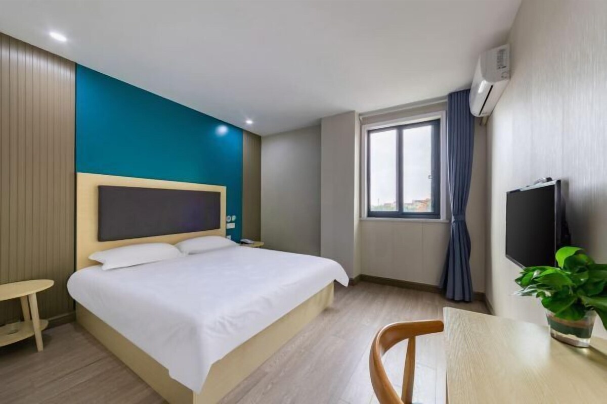 A hotel room with a bed, a small table, a chair, a TV, and a window with curtains.