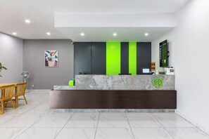 Uma área de recepção com balcão de mármore, esquema de cores verde e preto, e um espaço de estar com cadeiras.