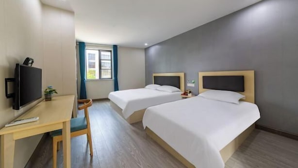 A hotel room with two beds, a desk with a chair, a television, and a window with curtains. - 99inn Selected Preferred Hotel (Shanghai Fengjing Ancient Town) (Shanghai)