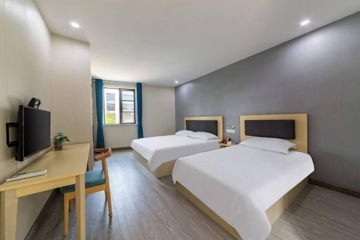 A hotel room with two beds, a desk with a chair, a television, and a window with curtains.