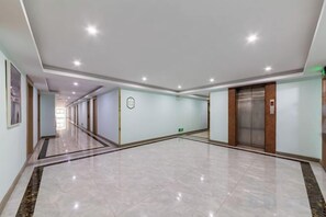 Corredor amplo e bem iluminado, com piso de mármore, área de recepção com balcão e elevador.