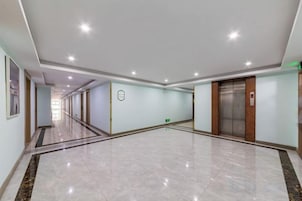 Un pasillo amplio y luminoso con suelo de mármol, una zona de recepción con mostrador y un ascensor.