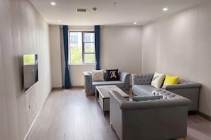 Ein modernes Wohnzimmer mit einem grauen Ecksofa, einem flachbildfernseher an der Wand und einem Fenster mit blauen Vorhängen.
