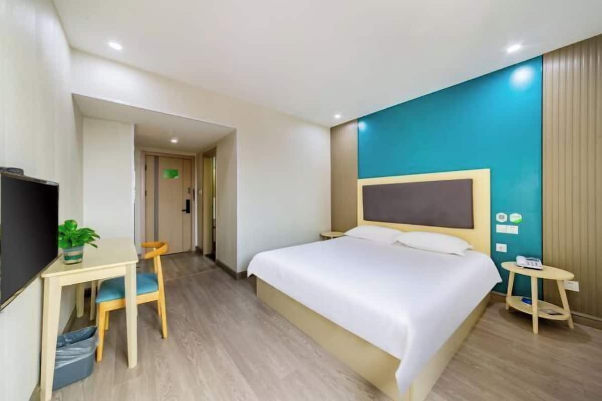 A hotel room with a bed, a desk with a chair, a television, and a small table with a plant.
