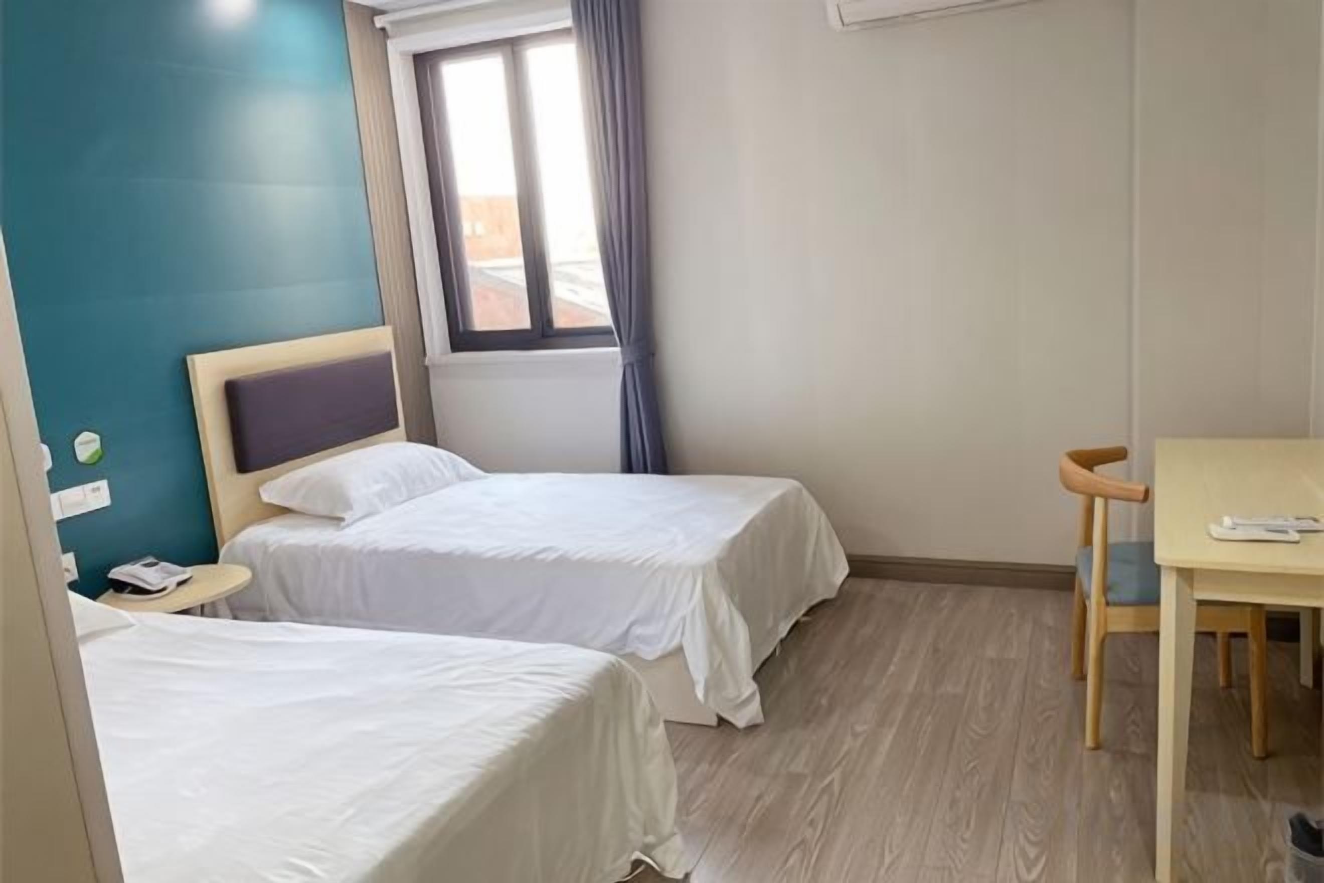 Habitación de hotel con dos camas, una mesa de madera, una ventana con cortinas y una mesita de noche pequeña.