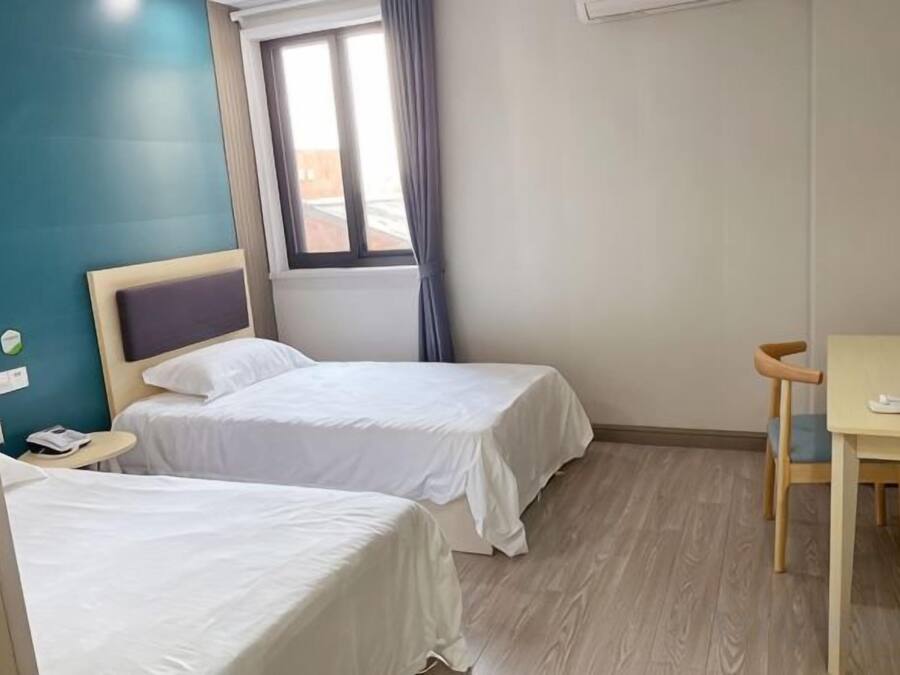 Habitación de hotel con dos camas, una mesa de madera, una ventana con cortinas y una mesita de noche pequeña.