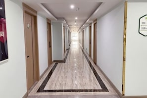 A long, narrow hotel corridor with doors on both sides, a tiled floor, and a sign on the right wall. - 99inn Selected Preferred Hotel (Shanghai Fengjing Ancient Town) (Shanghai)