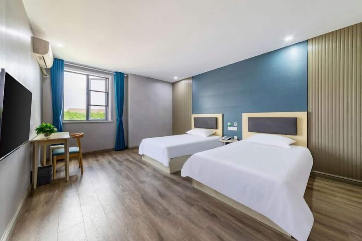 A hotel room with two beds, a desk with a chair, a TV, and a window with curtains.