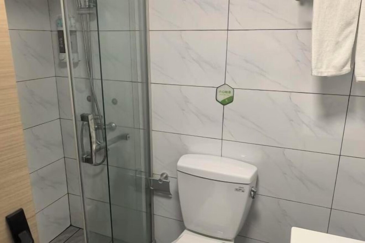A bathroom with a glass shower enclosure, a toilet, and a towel hanging on the wall.