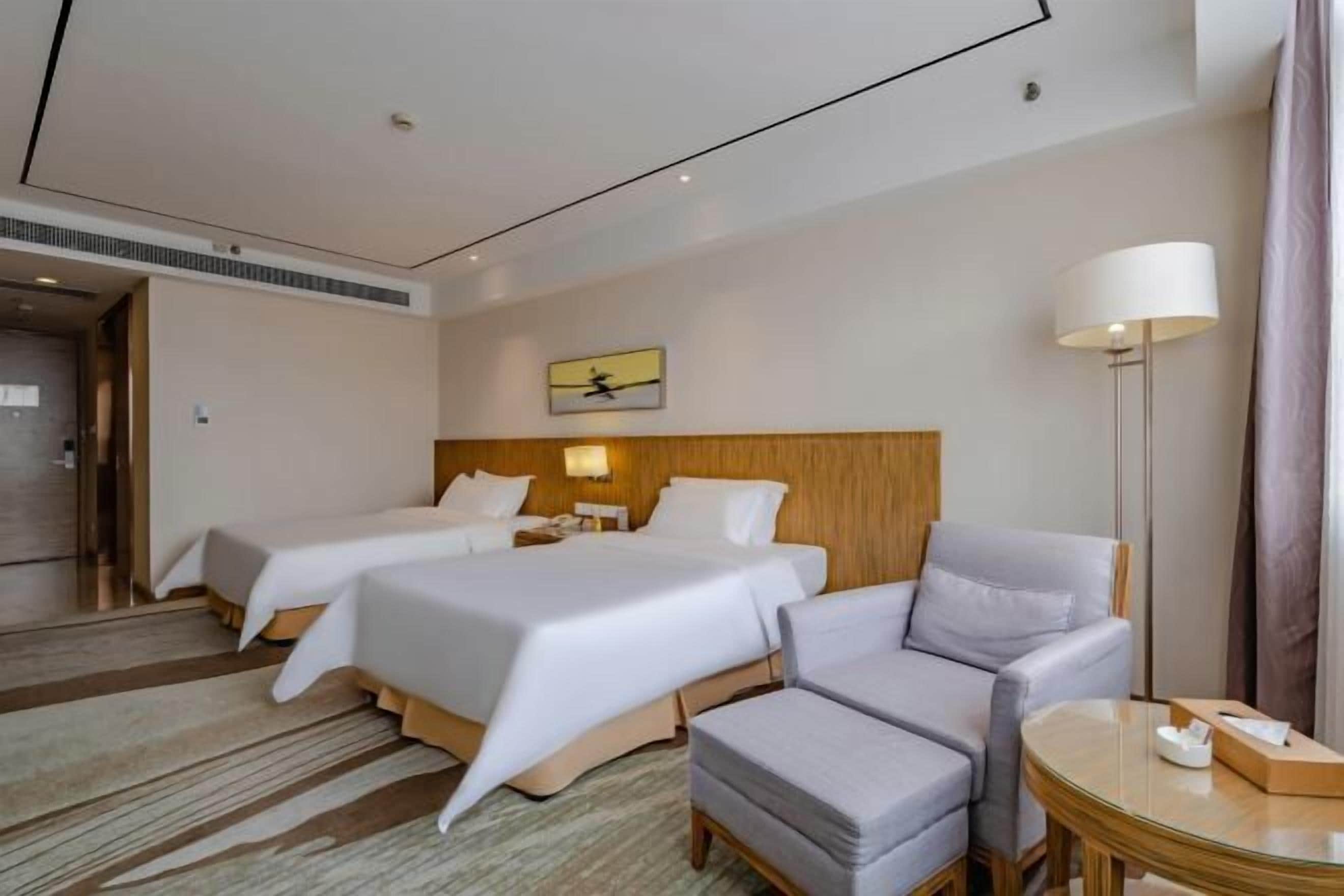 Habitación de hotel con dos camas, un sofá, una mesita y una lámpara.