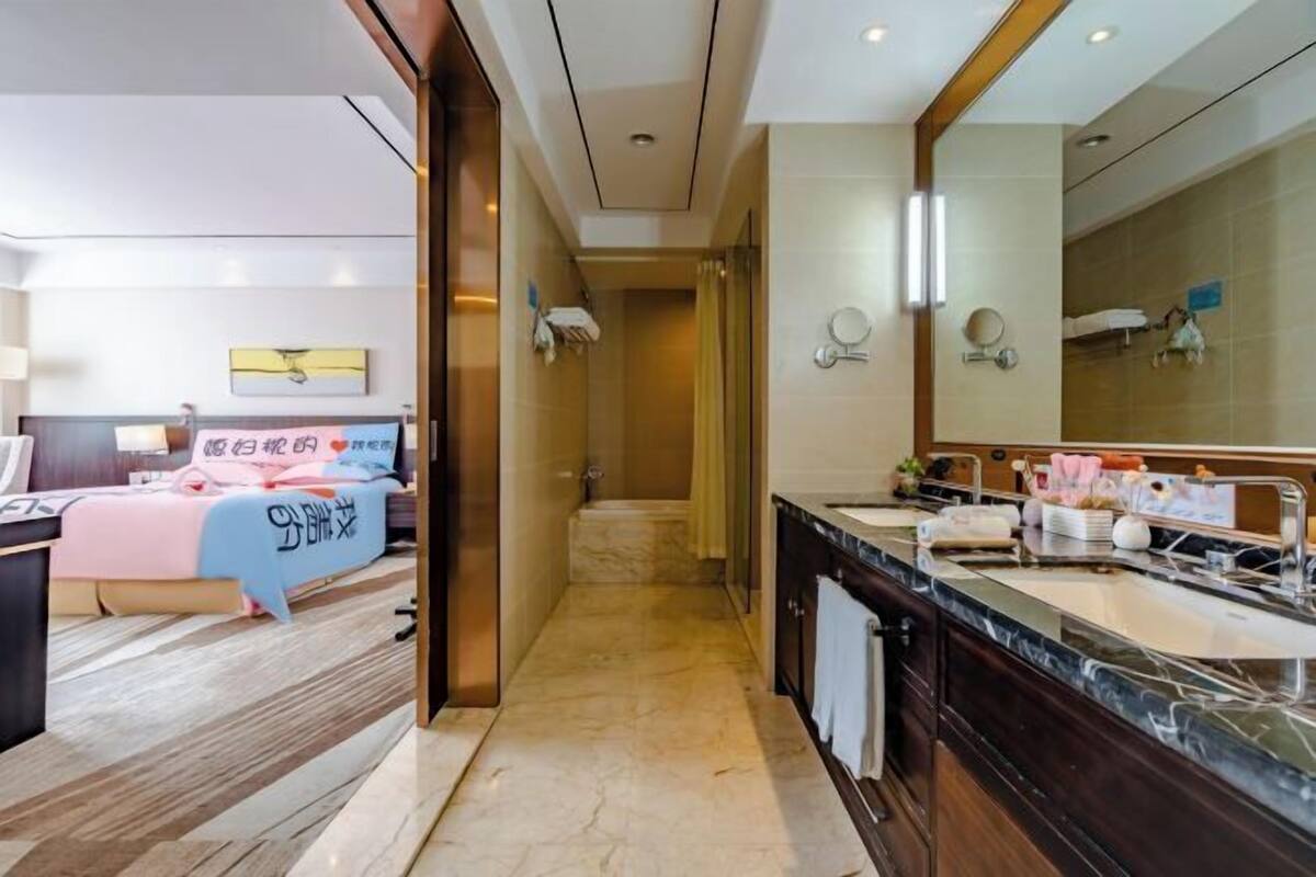 A hotel room with a bed, a bathroom with a large mirror, a sink, and a shower.