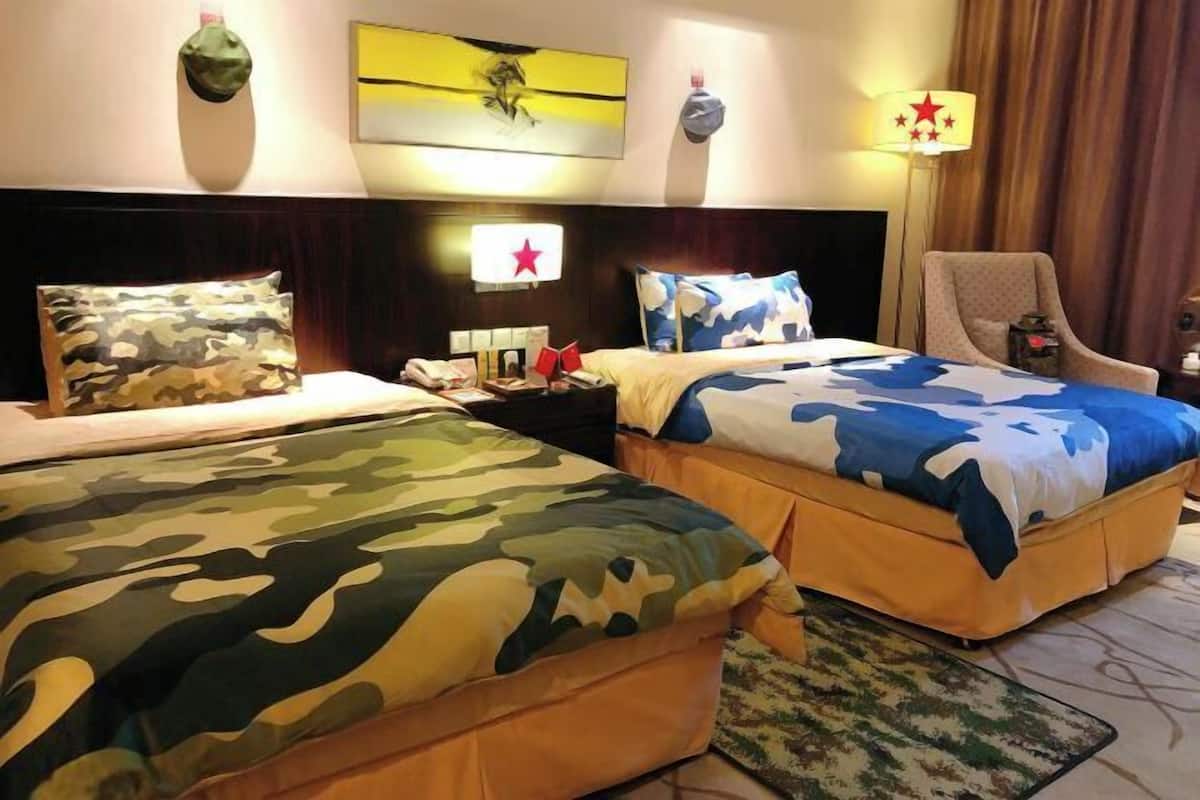 A hotel room with two beds, a nightstand, a lamp, and a chair.