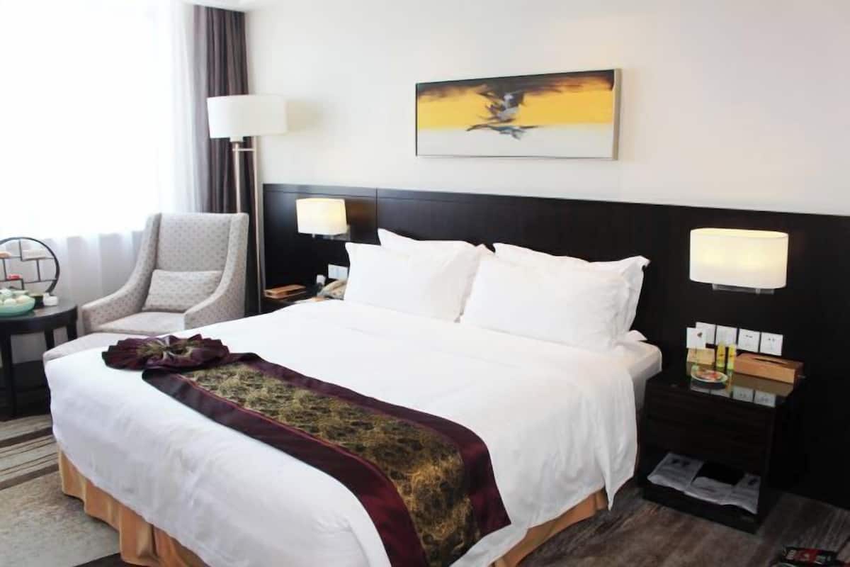 A hotel room with a large bed, two bedside tables, a chair, a painting on the wall, and a lamp.