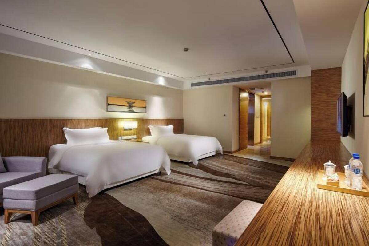 A hotel room with two beds, a sofa, a desk with a lamp, and a large rug.