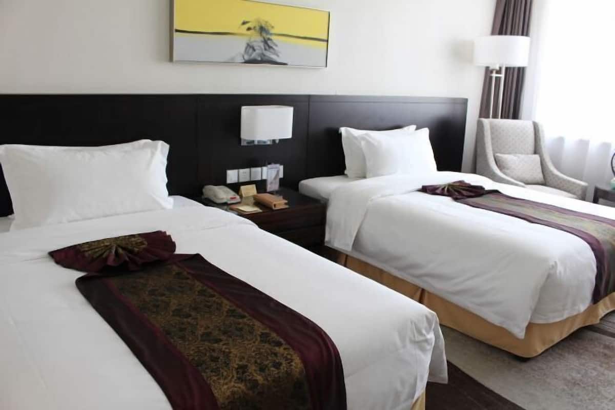 A hotel room with two beds, a nightstand with a phone and a lamp, a chair, and a painting on the wall.