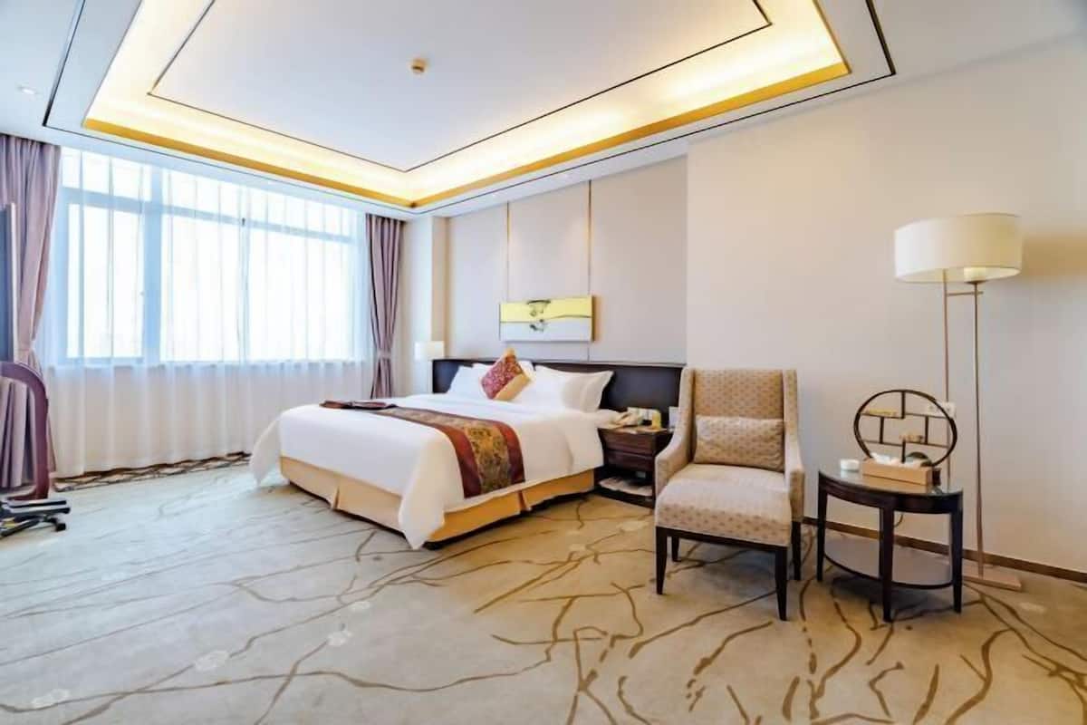A hotel room with a bed, a chair, a nightstand, a lamp, and a window with curtains.