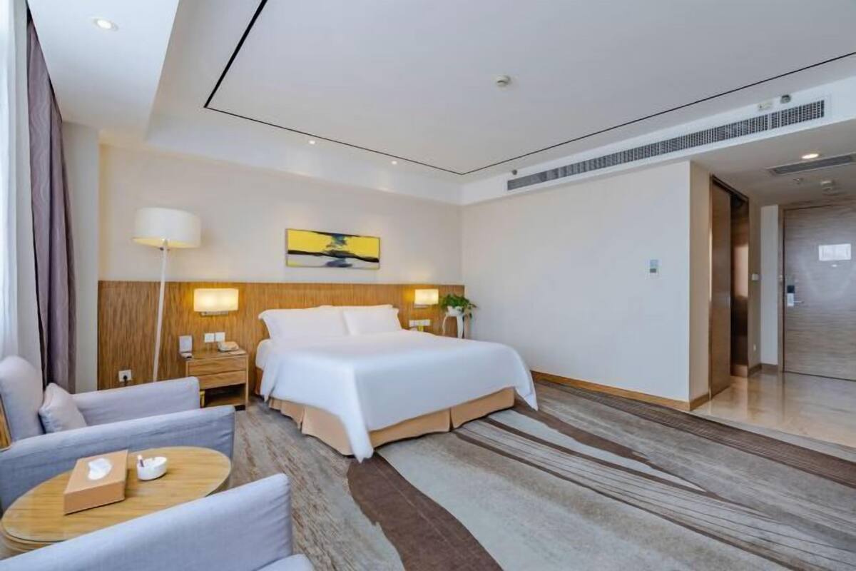 A modern hotel room with a large bed, a desk, a chair, and a small table.