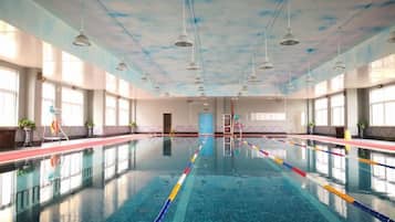 A large indoor swimming pool with clear lanes, a tiled floor, and a high ceiling with hanging lights.