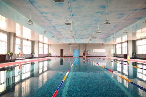 A large indoor swimming pool with clear lanes, a tiled floor, and a high ceiling with hanging lights.