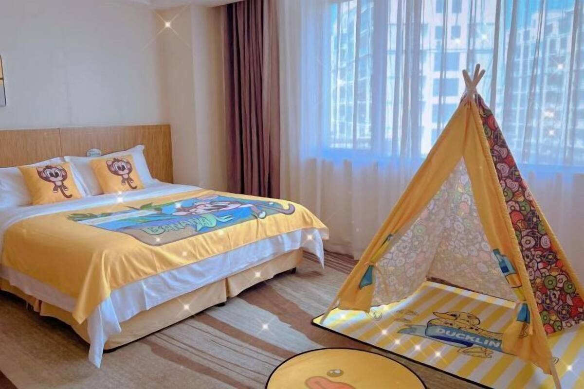 A hotel room with a bed, a window with curtains, and a teepee with a duckling design.