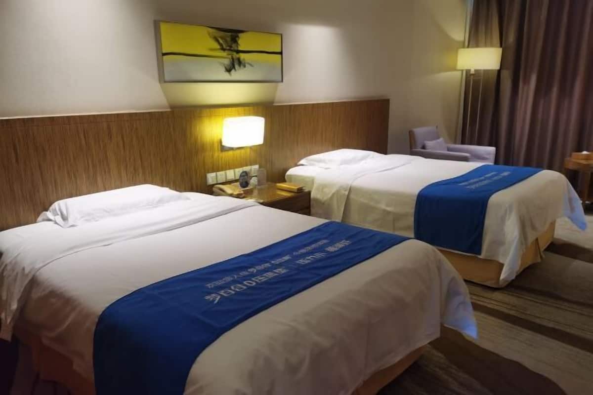 A hotel room with two beds, a nightstand, a lamp, a chair, and a painting on the wall.