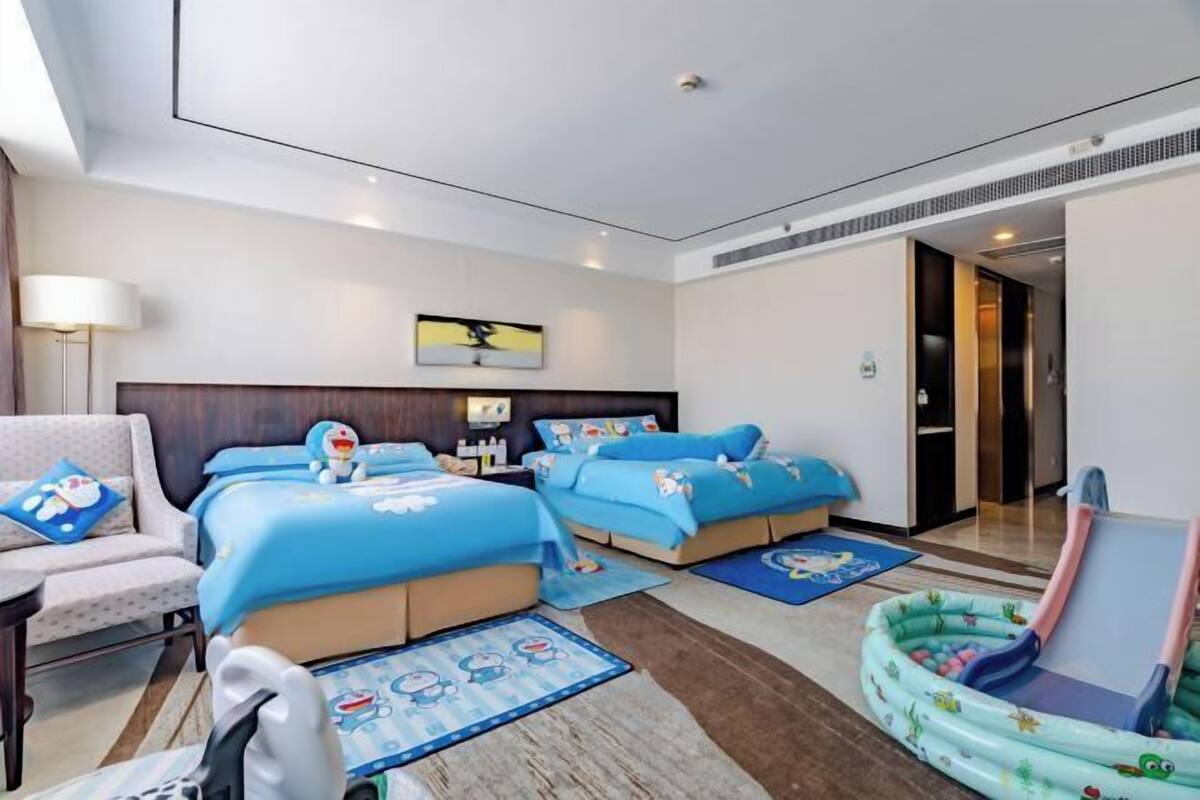 A hotel room with two beds, a chair, a desk, a lamp, a painting, and a small inflatable pool.