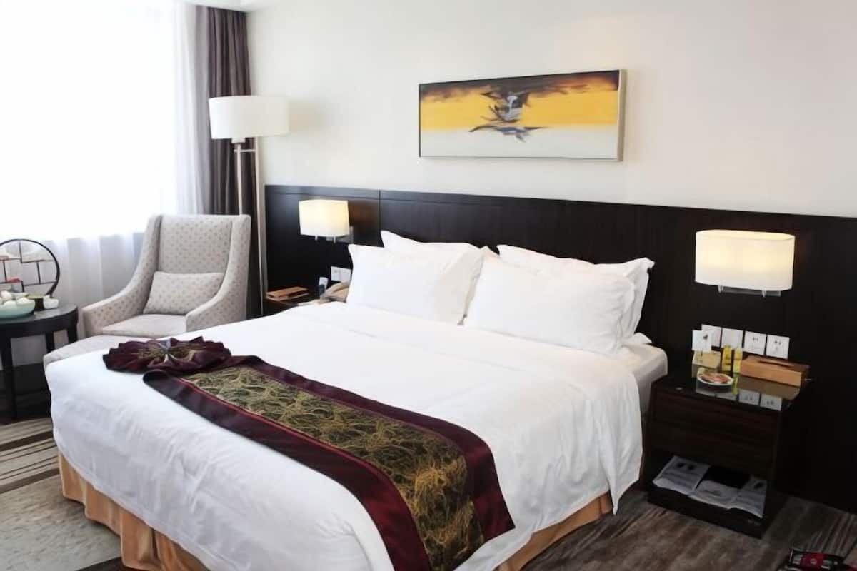 A hotel room with a large bed, two bedside lamps, a chair, a nightstand, and a painting on the wall.