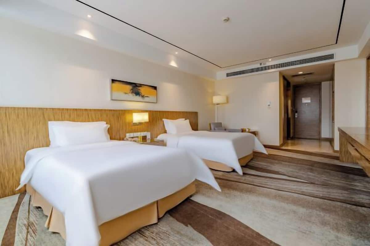 A hotel room with two beds, a wooden headboard, a painting on the wall, and a lamp on the nightstand.