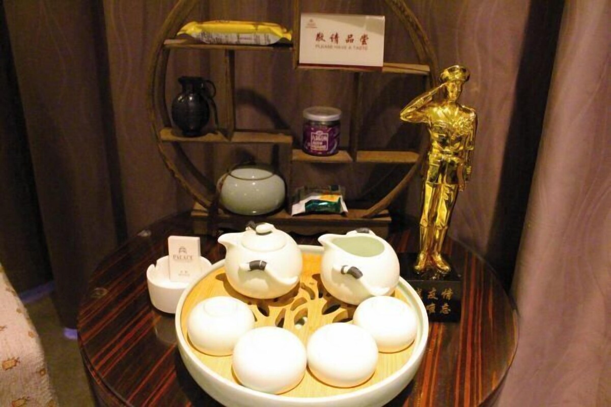A traditional tea set with teapots and cups on a wooden tray, a golden statue, and a shelf with various items in the background.