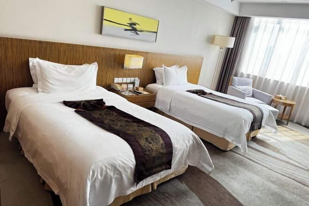 A hotel room with two beds, a wooden headboard, a painting, a lamp, and a view of the outdoors through the window.